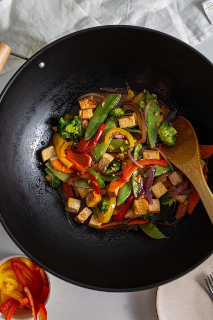 Teriyaki tofu and vegetable stir fry in a wok with a wooden spoon.