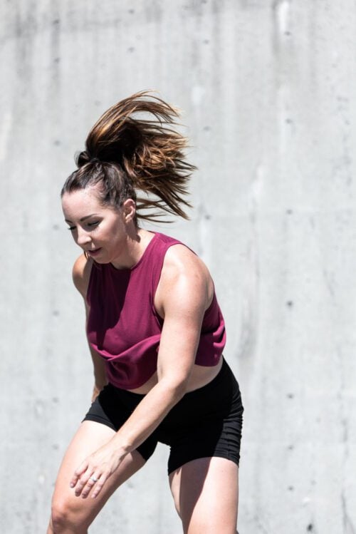 A fit woman in athletic clothing performing a skater jump.