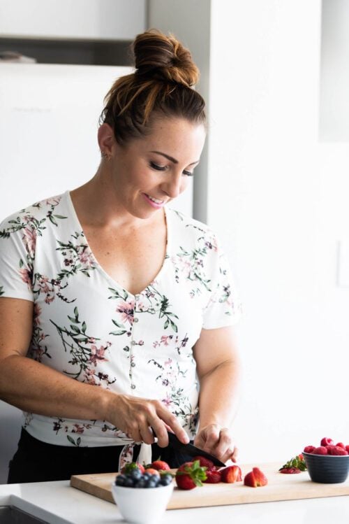 A woman in a floral shirt cutting fruit on a kitchen island.