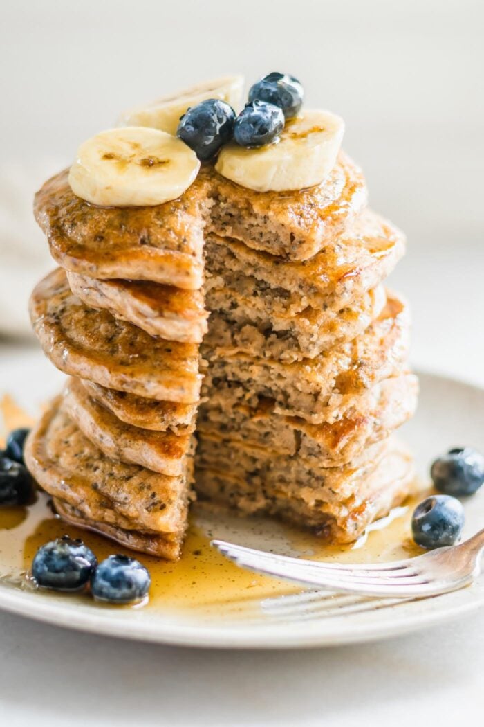 Stack of fluffy pancakes that's been cut into so you can see the inside texture of them. They're topped with blueberries and banana.