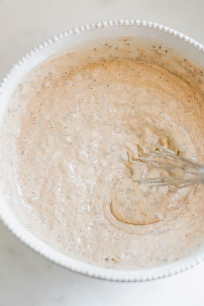 Thick chia seed pancake batter in a glass mixing bowl with a whisk.