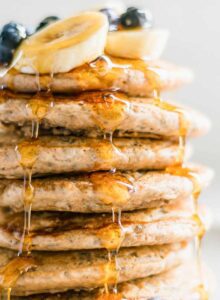 Stack of 7 thick and fluffy chia pancakes topped with maple syrup and blueberries on a plate.