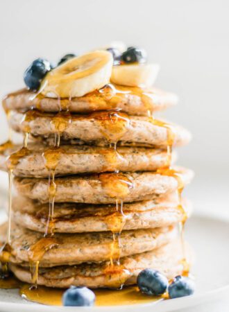 Stack of 7 thick and fluffy chia pancakes topped with maple syrup and blueberries on a plate.