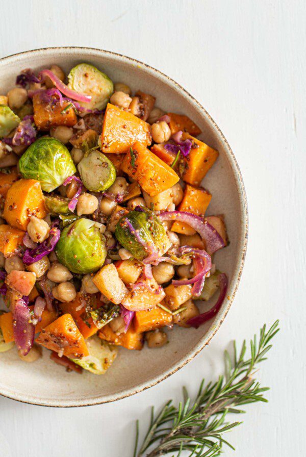 Overhead view of a dish of chickpeas, sweet potato, Brussels sprouts, cabbage and red onion in maple dijon sauce.