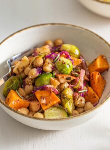 Small dish of chickpeas, sweet potato, Brussels sprouts, cabbage and red onion in maple dijon sauce.