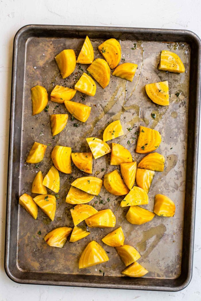 Chopped and peeled golden beets on a baking pan drizzled with olive oil.
