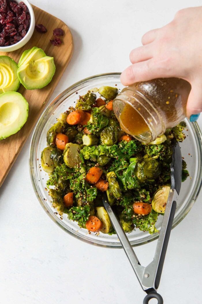 Pouring dressing over a kale, carrot and brussels spout salad with quinoa.