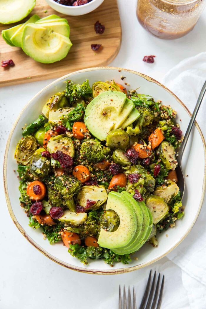 Kale quinoa salad with cranberries and roasted vegetables topped with avocado in a bowl.