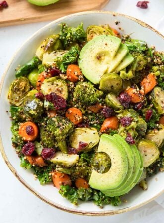 Kale quinoa salad with cranberries and roasted vegetables topped with avocado in a bowl.