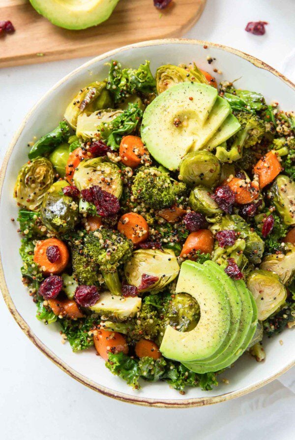 Kale quinoa salad with cranberries and roasted vegetables topped with avocado in a bowl.