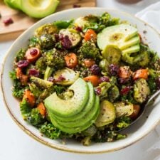 Kale quinoa salad with cranberries and roasted vegetables topped with avocado in a bowl.