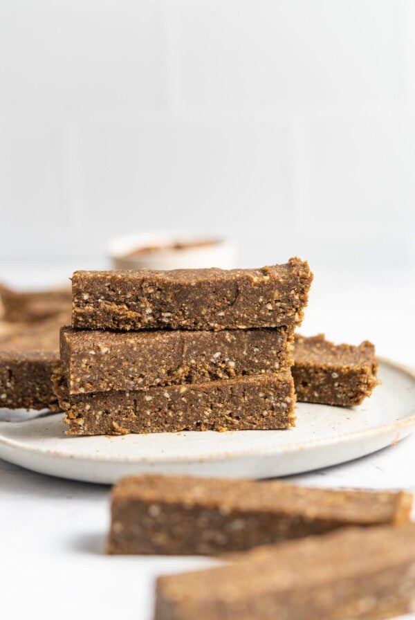 Stack of 3 hemp protein energy bars on a plate with more bars scattered around in the background.