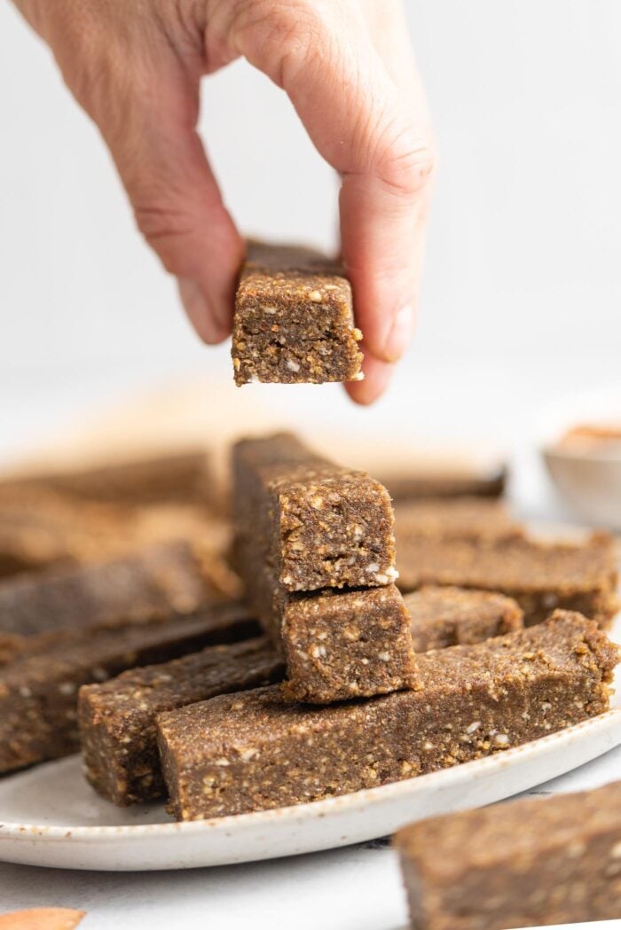 Hand lifting a hemp protein bar from a stack of bars on a plate.