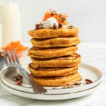 Stack of 6 thick carrot pancakes on a small plate. Fork rests on the plate.