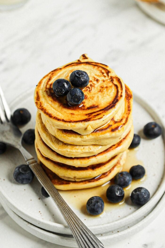 Stack of 6 thick chickpea flour pancakes topped with blueberries and maple syrup on a small plate.