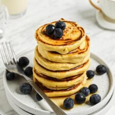 Stack of 6 thick chickpea flour pancakes topped with blueberries and maple syrup on a small plate.