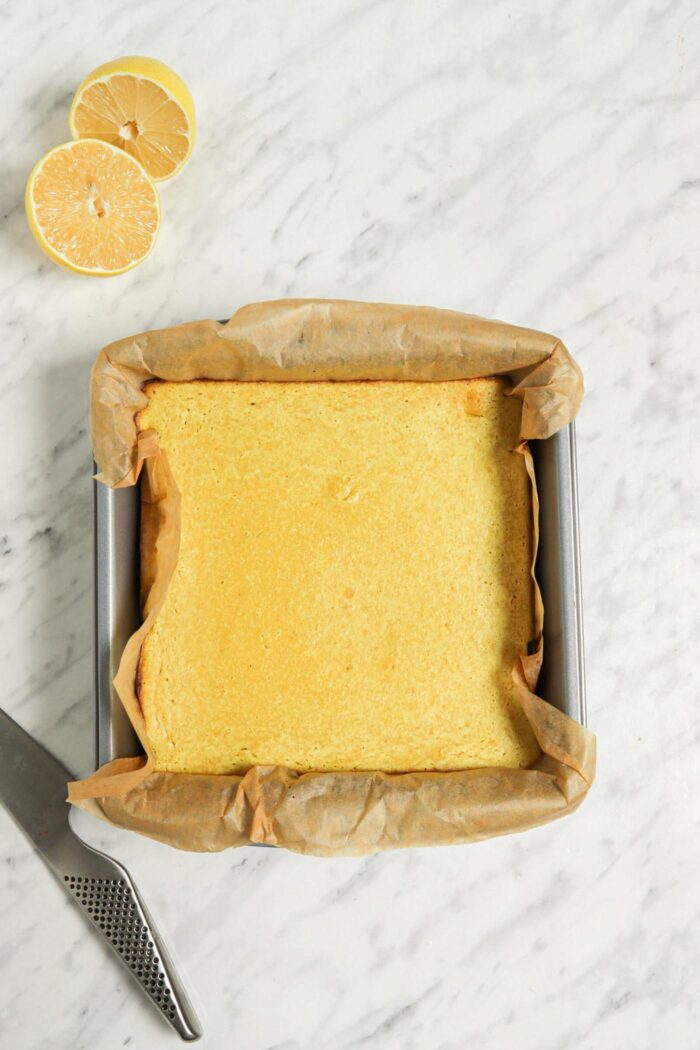 Vegan lemon bars in a square metal baking pan lined with parchment paper.