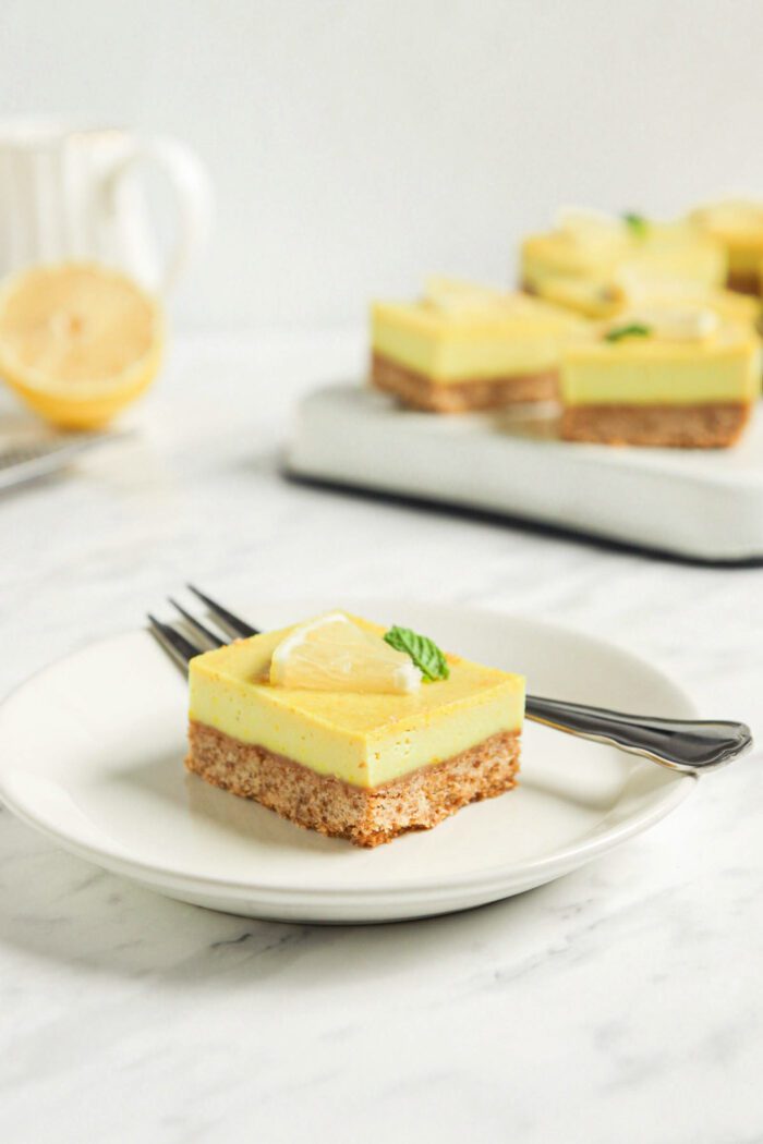 One creamy vegan lemon bar on a small white plate with a fork.