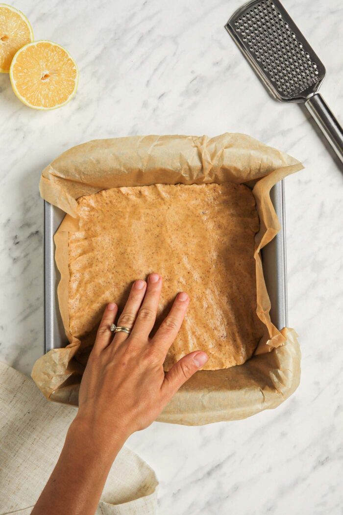 Hand pressing dough into a parchment paper-lined baking dish.