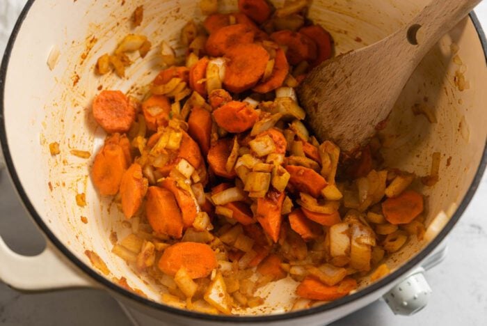 Onion, garlic and carrot cooking in spices with tomato paste in a large soup pot.