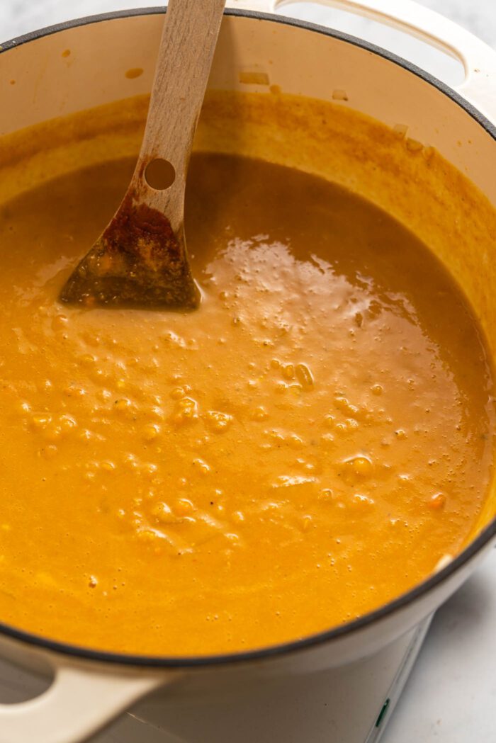 Lemon red lentil soup with turmeric in a soup pot with a wooden spoon.