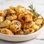 Bowl of crispy roasted lemon rosemary potatoes with a sprig of rosemary resting in the bowl.