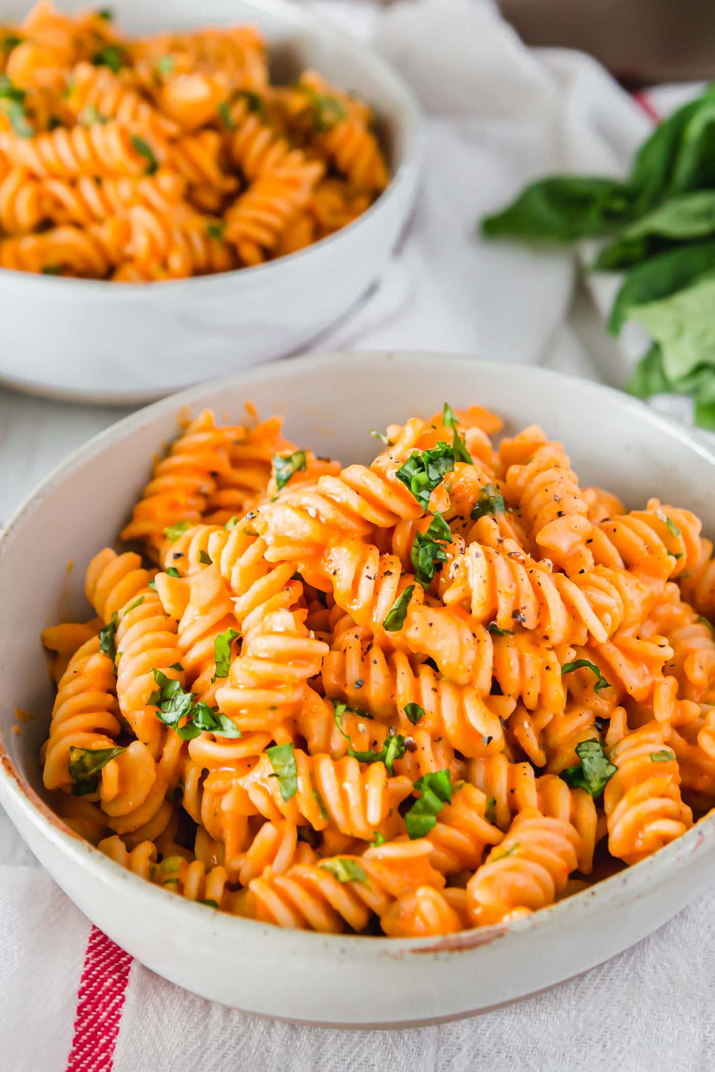 A bowl of vegan roasted red pepper pasta topped with chopped fresh herbs.