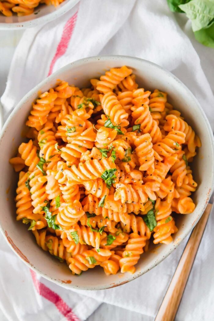 Overhead view of a bowl of vegan roasted red pepper pasta topped with chopped fresh herbs.