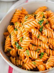 A bowl of vegan roasted red pepper pasta topped with chopped fresh herbs.