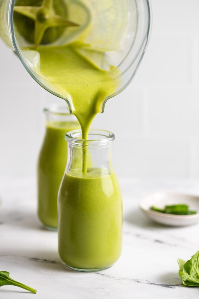 Pouring a green mango smoothie from a blender into a small jar.
