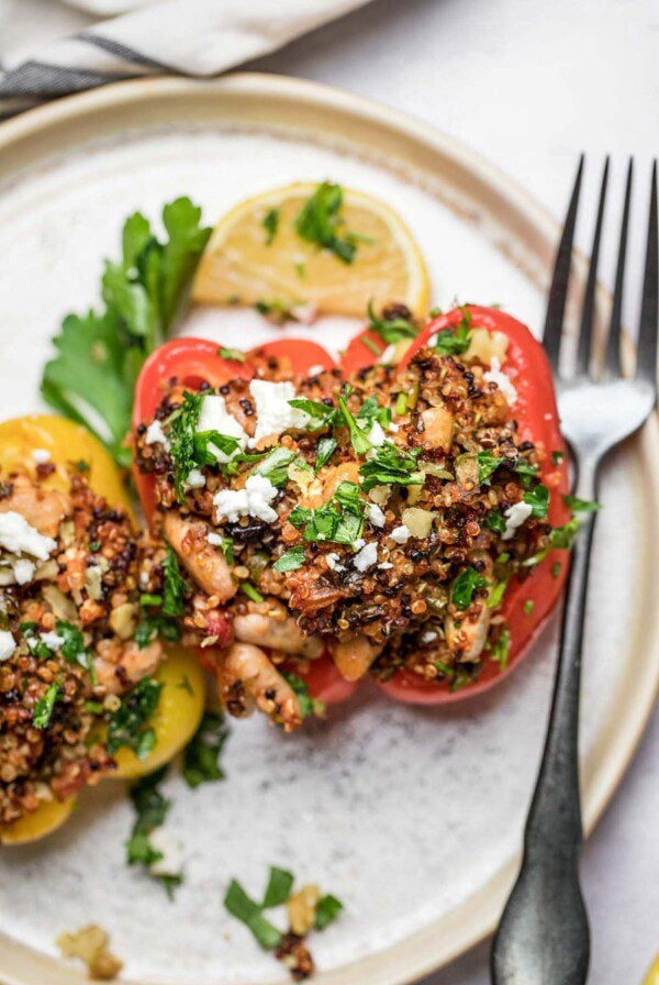 Two Mediterranean quinoa stuffed bell peppers topped with feta and parsley on a plate.