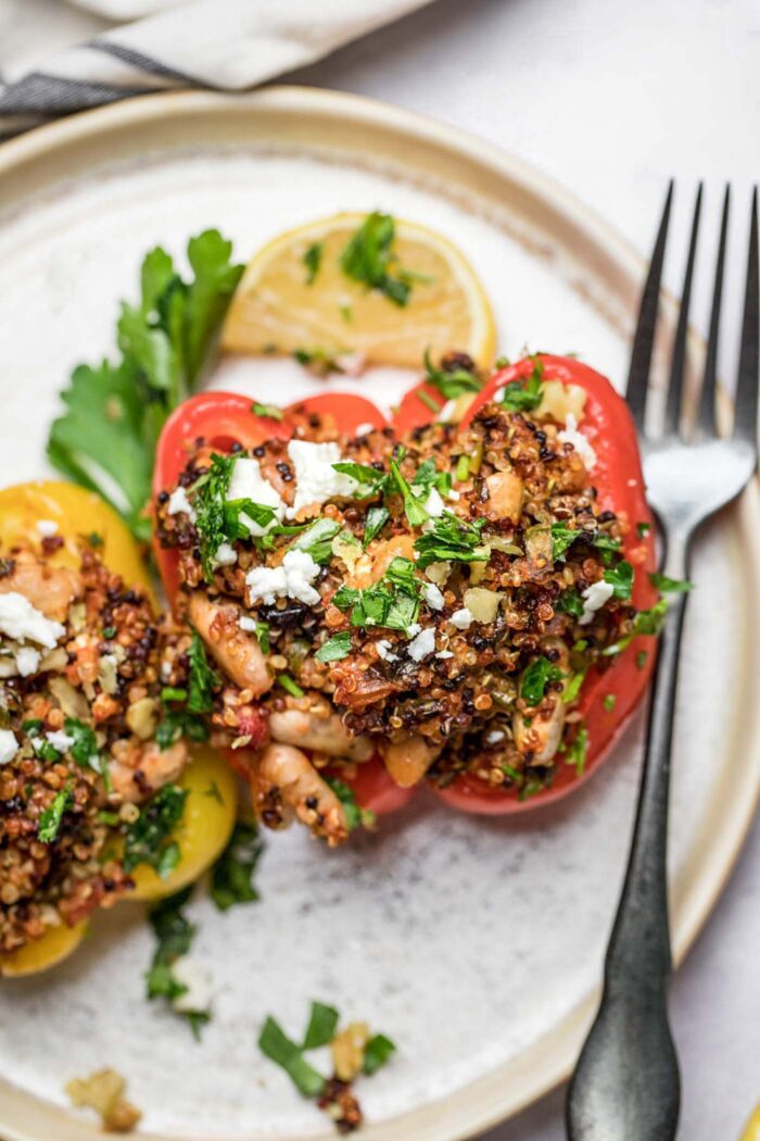 Two Mediterranean quinoa stuffed bell peppers topped with feta and parsley on a plate.