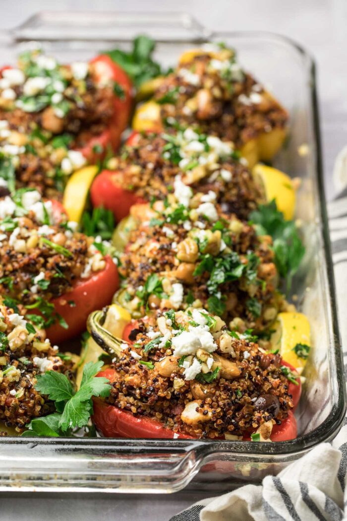 A casserole dish of halved stuffed bell peppers filling with a quinoa and bean mixture and topped with feta.
