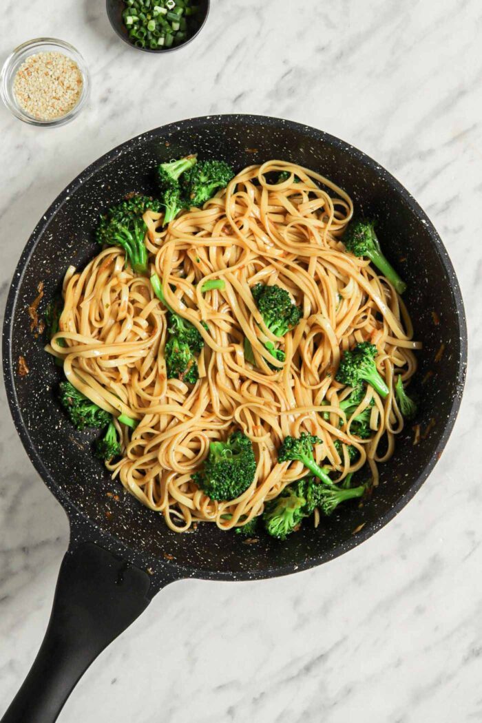 Noodles with broccoli cooking in a skillet.