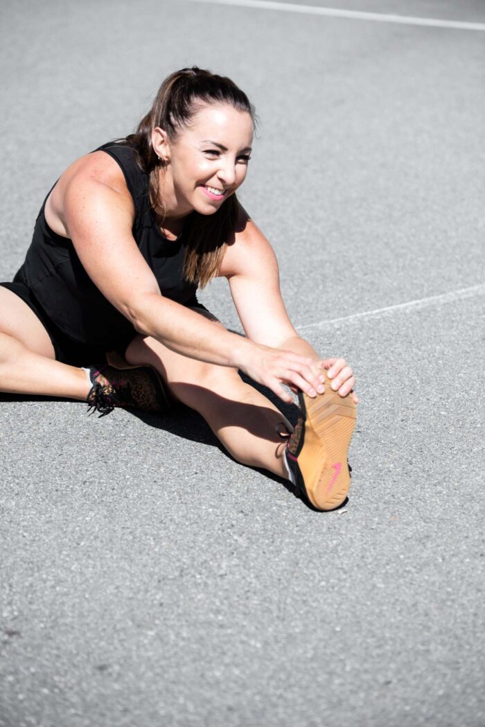 A fit woman performing a hamstring stretch on a concrete surface.