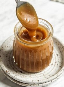 Spoon dipping into a small jar of homemade vegan caramel sauce.