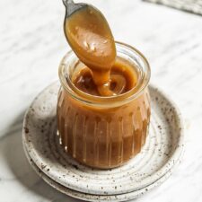 Spoon dipping into a small jar of homemade vegan caramel sauce.