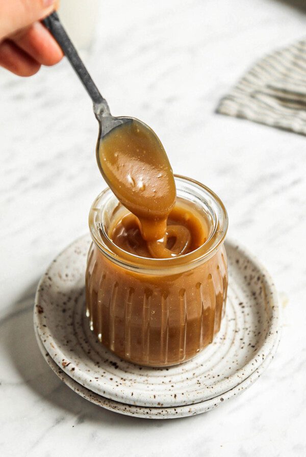 Spoon dipping into a small jar of homemade vegan caramel sauce.