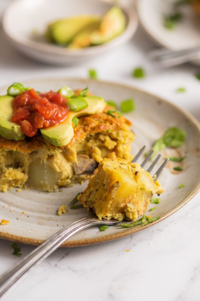 Forkful of vegan potato egg breakfast casserole on a plate beside a slice of casserole.