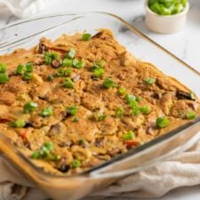 Baked vegan potato egg casserole in a glass baking dish. Small dish of sliced avocado is in the background.