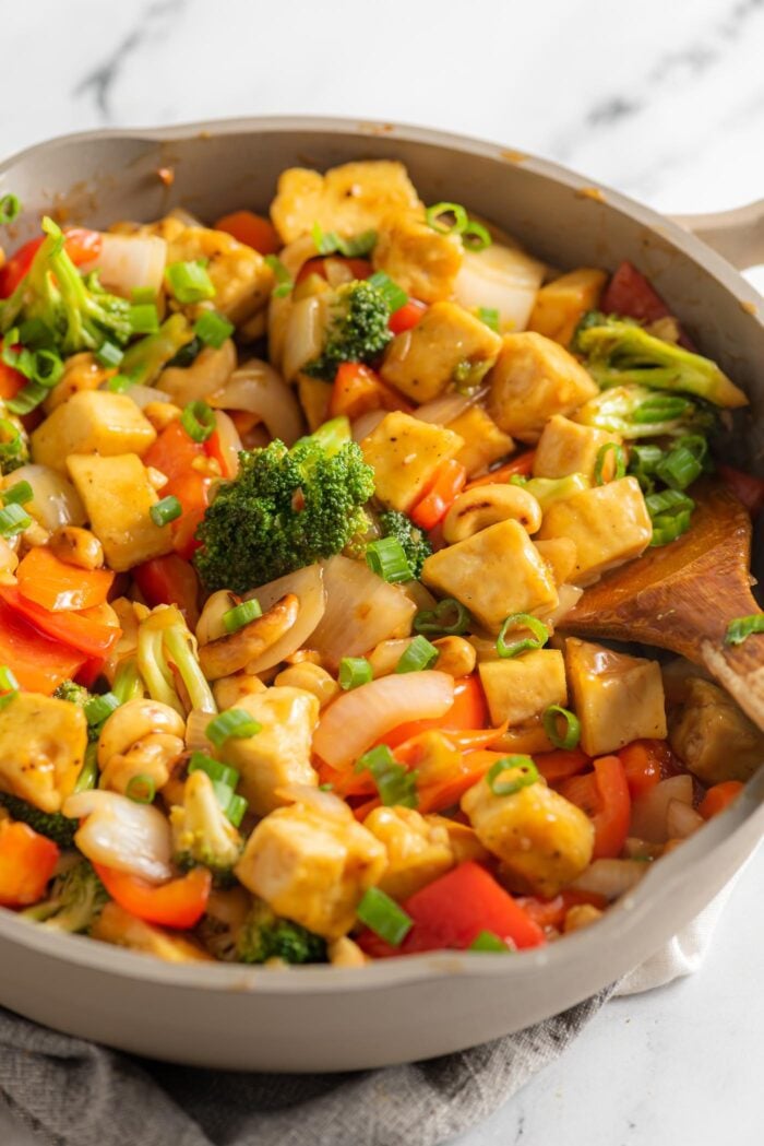 A cashew tofu broccoli stir fry in a large skillet on a marble surface.