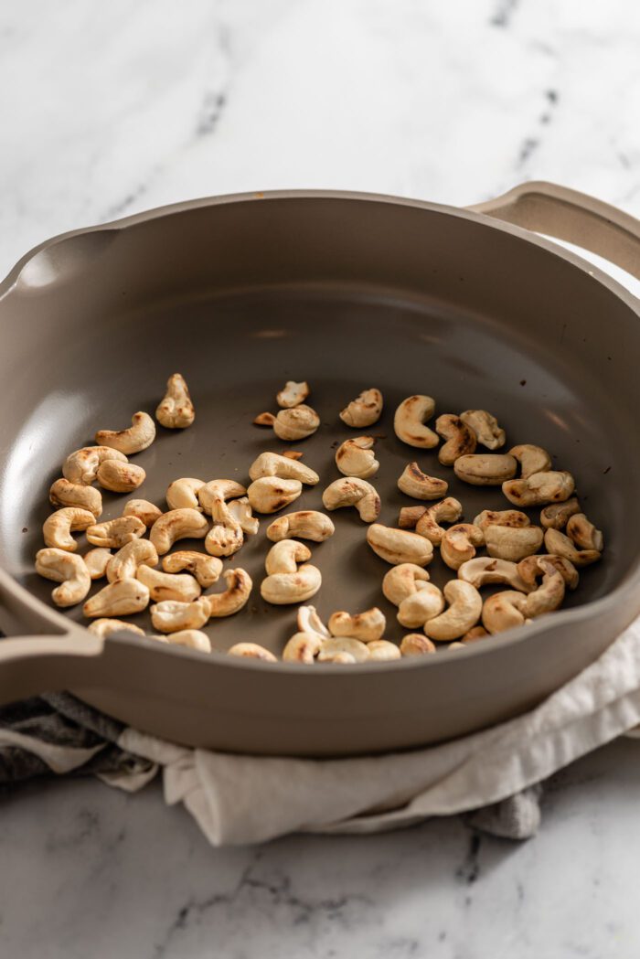 Raw cashews toasting in a skillet.