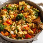A cashew tofu vegetable stir fry in a large skillet on a marble surface.
