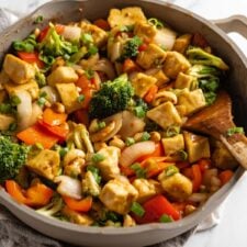 A cashew tofu vegetable stir fry in a large skillet on a marble surface.