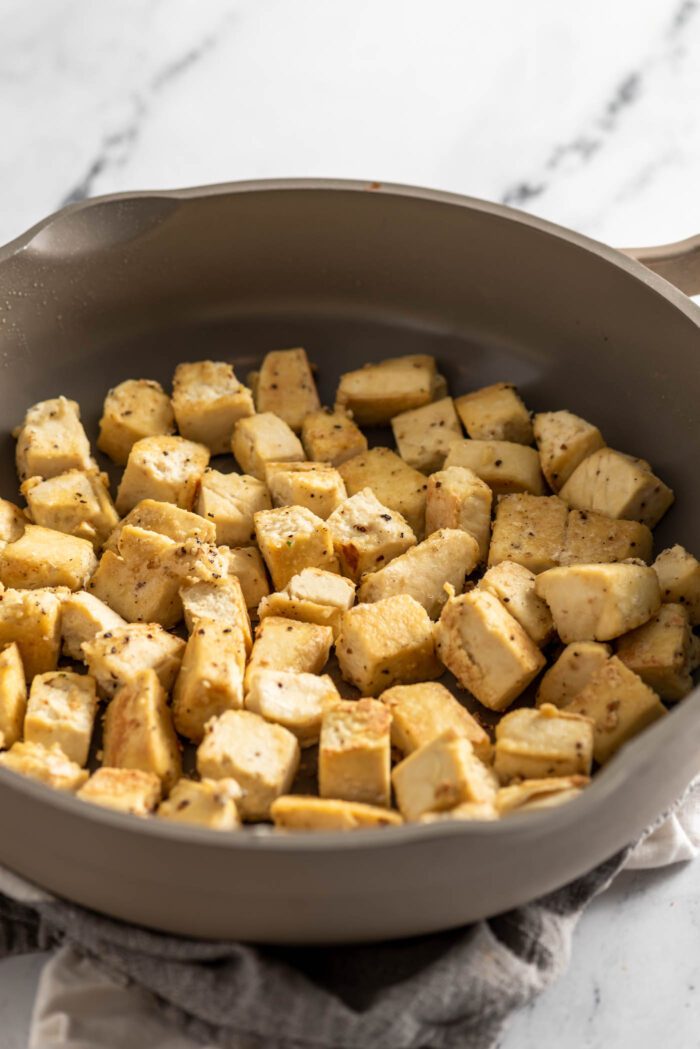 Browned cubes of tofu frying in a skillet.