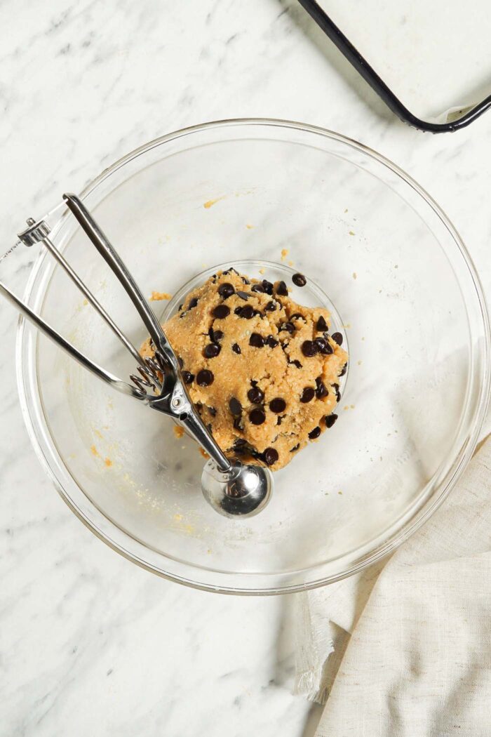 Chocolate chip almond flour cookie dough in a glass mixing bowl with a cookie scoop.