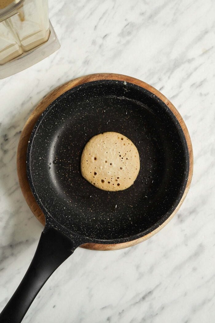 A vegan and gluten-free oat banana pancake cooking in a small nonstick pan.