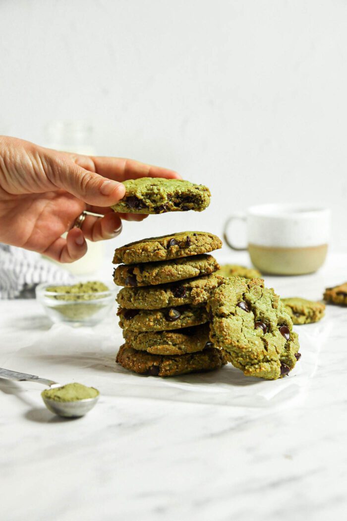 Hand taking a matcha green tea cookie from a stack of cookies on a marble surface.