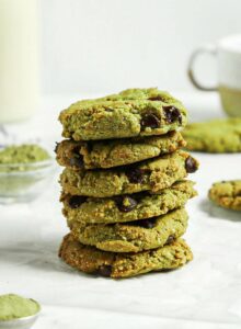Stack of almond flour matcha chocolate chip cookies. There's a glass of milk in the background and a tablespoon of matcha powder in the foreground.