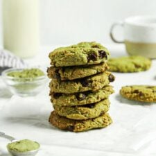 Stack of almond flour matcha chocolate chip cookies. There's a glass of milk in the background and a tablespoon of matcha powder in the foreground.